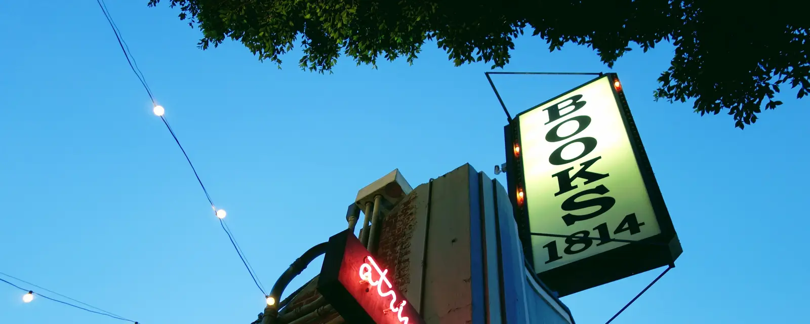 A bookshop's neon sign under string lights at dusk